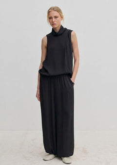 A person wearing a sleeveless black turtleneck top and matching black Nya Pants with an elasticated waist and loose-fitting, balloon leg silhouette.