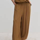 Person wearing brown Nya Pants with a balloon leg, elastic waistband, and tucked-in matching top, paired with off-white shoes.