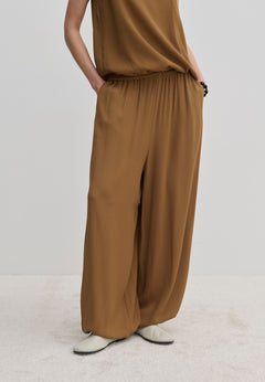 Person wearing brown Nya Pants with a balloon leg, elastic waistband, and tucked-in matching top, paired with off-white shoes.