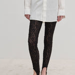 Person wearing a white button-down shirt, slim-fit black stretch-lace Ringo Leggings with stirrup straps, and black flat shoes.