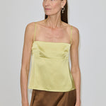 A woman wearing a pale yellow Angela Top with a square neckline and a brown skirt.