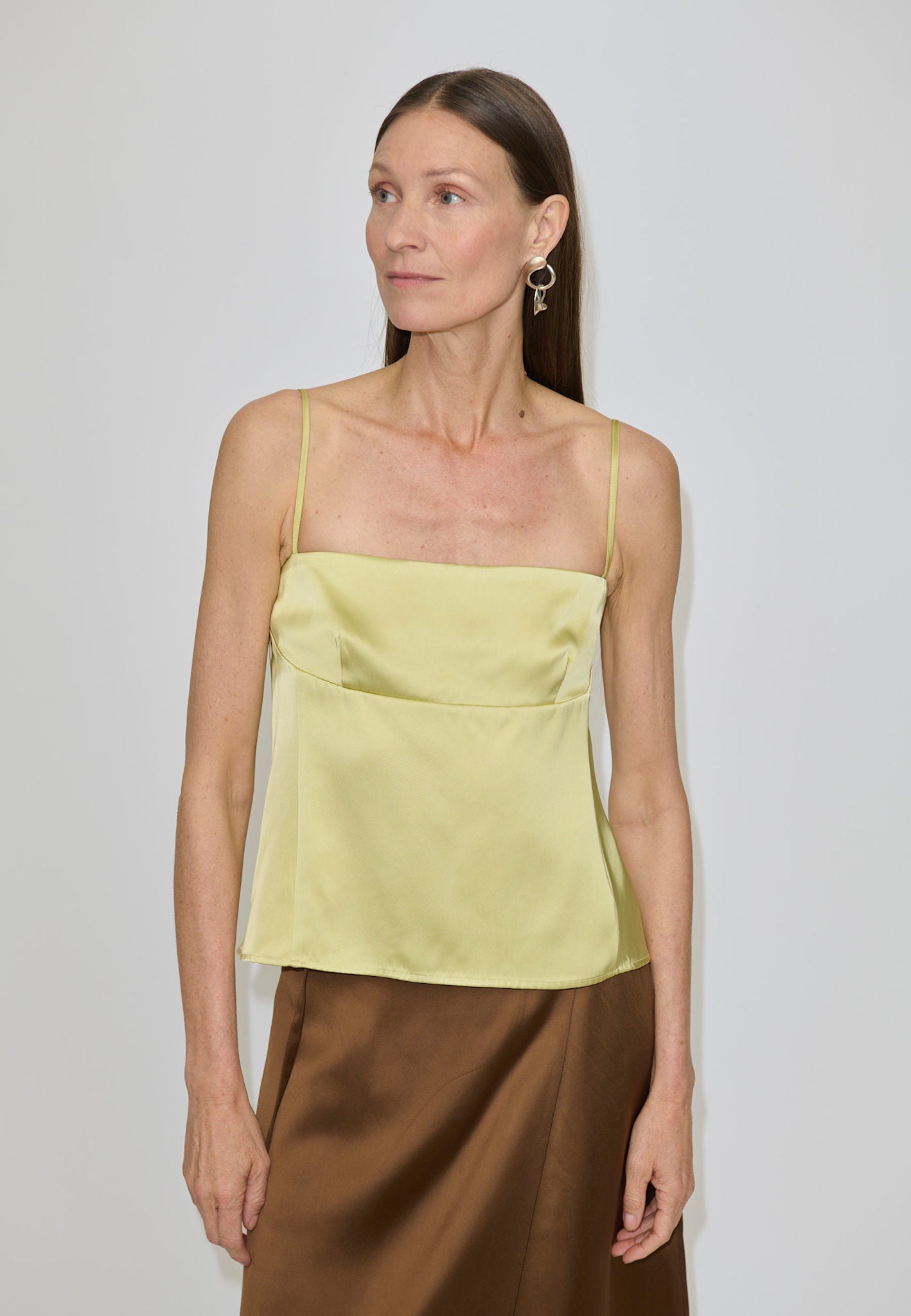 A woman wearing a pale yellow Angela Top with a square neckline and a brown skirt.