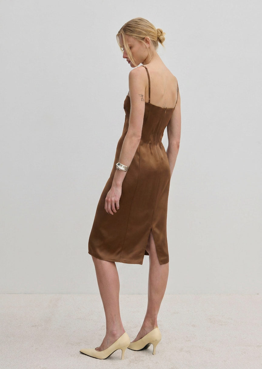 A woman wears a brown Herskind ApS Amina dress, a midi-length FSC Viscose slip dress with adjustable straps and a back vent, paired with light-colored high heels.