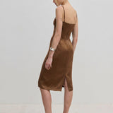A woman wears a brown Herskind ApS Amina dress, a midi-length FSC Viscose slip dress with adjustable straps and a back vent, paired with light-colored high heels.