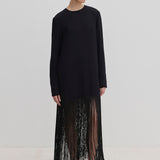 The Aris Dress by Herskind ApS is a long-sleeved black shift dress with a crew neckline and an ankle-length fringe hem, styled with black mules.