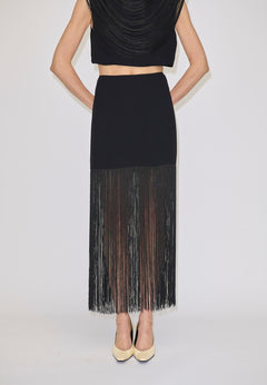 The Herskind ApS Olivia Skirt is a black high-waisted midi skirt with long, sheer fringe at the hem, worn with a matching sleeveless top and cream heels.