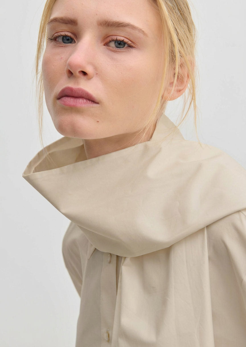 A woman wearing a beige Natalia Shirt by Herskind ApS, an oversized cotton button-down with a wide, structured mock-neck collar.