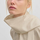 A woman wearing a beige Natalia Shirt by Herskind ApS, an oversized cotton button-down with a wide, structured mock-neck collar.