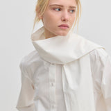 The Natalia Shirt by Herskind ApS is an oversized white cotton button-up with an attached scarf-like collar piece draped around the neck.