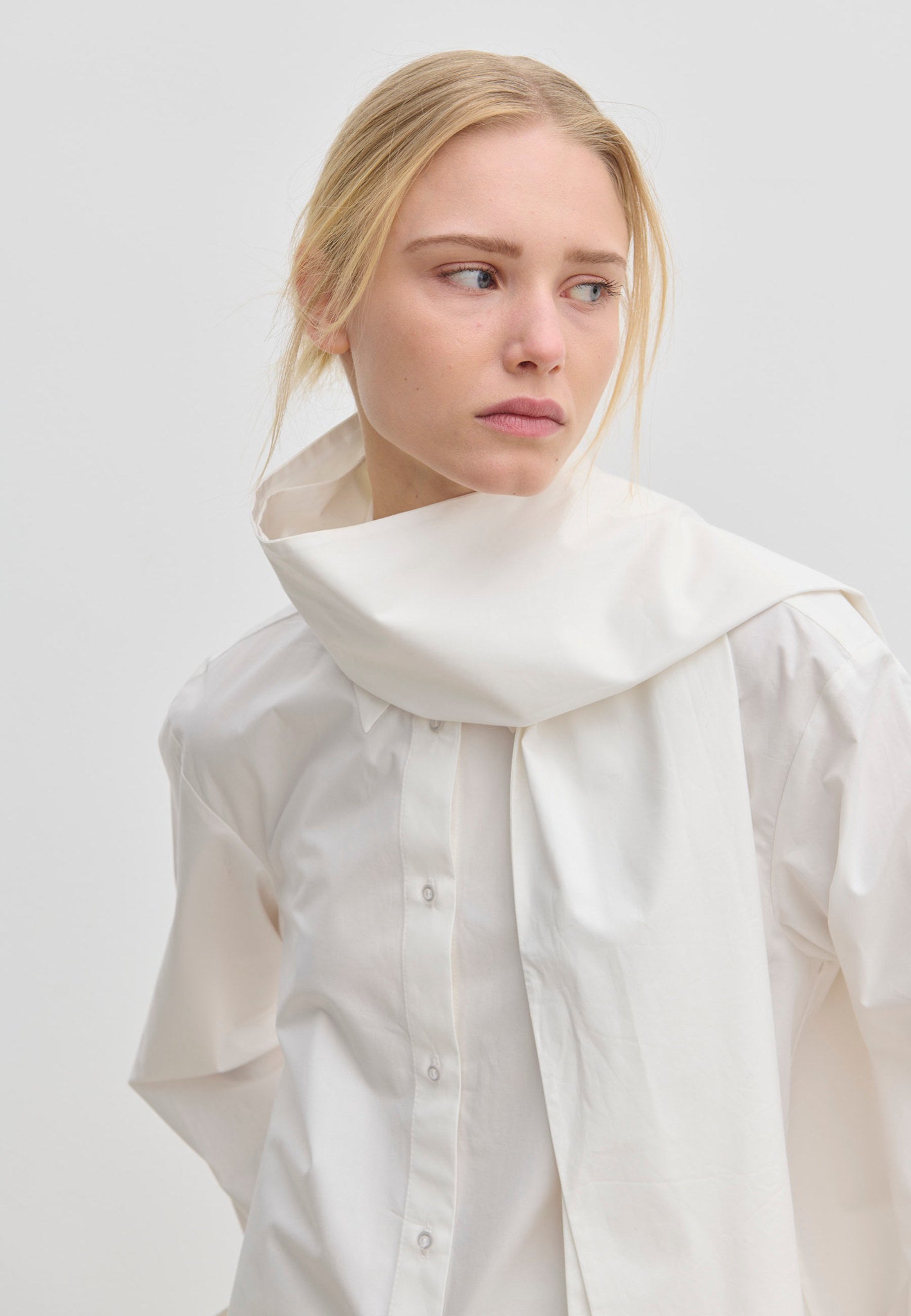 The Natalia Shirt by Herskind ApS is an oversized white cotton button-up with an attached scarf-like collar piece draped around the neck.