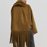 A person wearing a brown Daniella Scarf by Herskind ApS, oversized with long fringe draped over their shoulders.