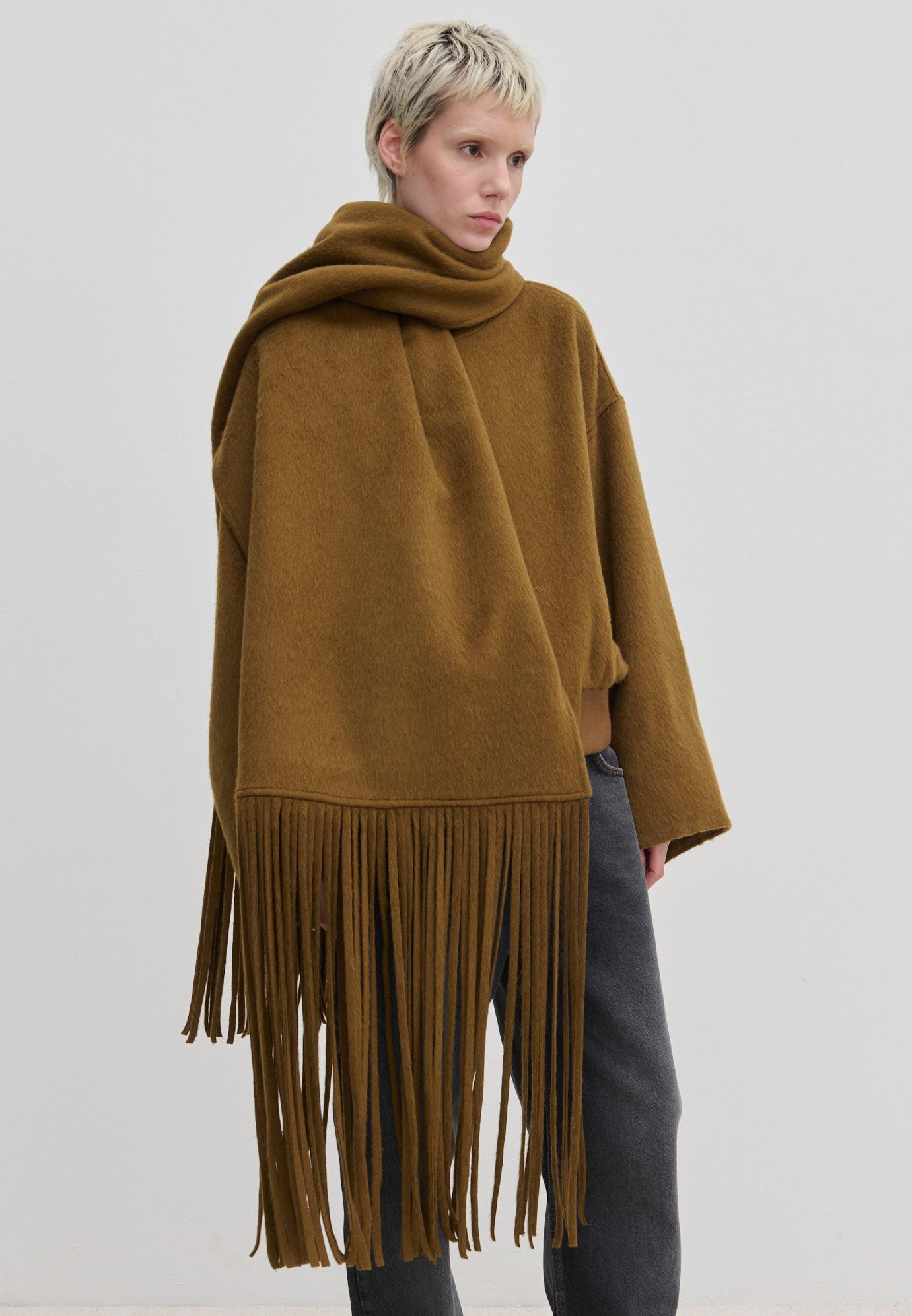 A person wearing a brown Daniella Scarf by Herskind ApS, oversized with long fringe draped over their shoulders.