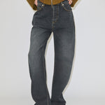 A person wears relaxed fit, dark grey Herskind ApS Antonie Denim Jeans (30 - Short) with contrast stitching and light-colored pointed-toe shoes.