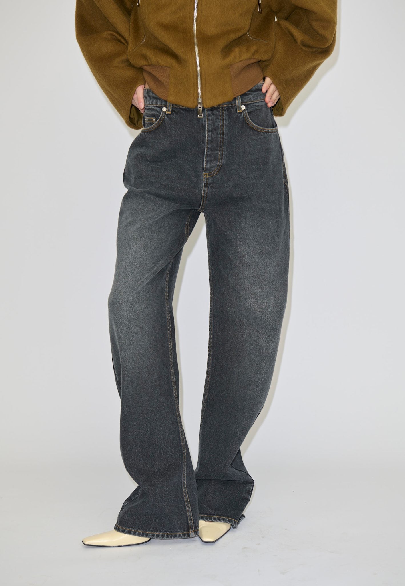 A person wears relaxed fit, dark grey Herskind ApS Antonie Denim Jeans (30 - Short) with contrast stitching and light-colored pointed-toe shoes.