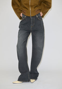 A person wears relaxed fit, dark grey Herskind ApS Antonie Denim Jeans (30 - Short) with contrast stitching and light-colored pointed-toe shoes.